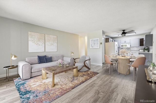 living area featuring light wood-style floors, ceiling fan, baseboards, and a textured ceiling