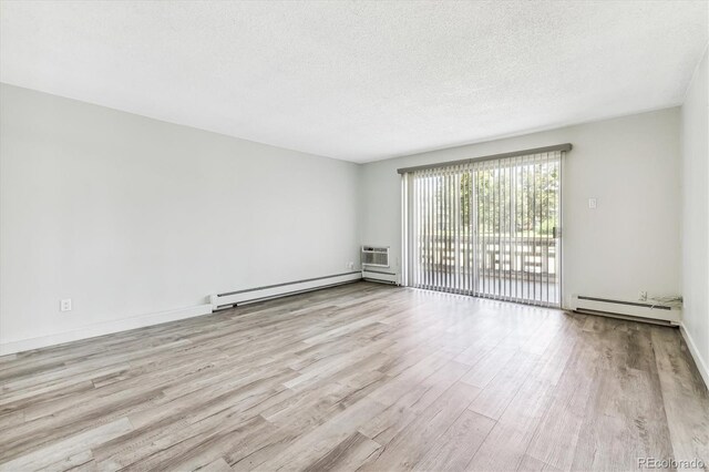 spare room with a wall mounted AC, a baseboard radiator, light wood-type flooring, and a textured ceiling