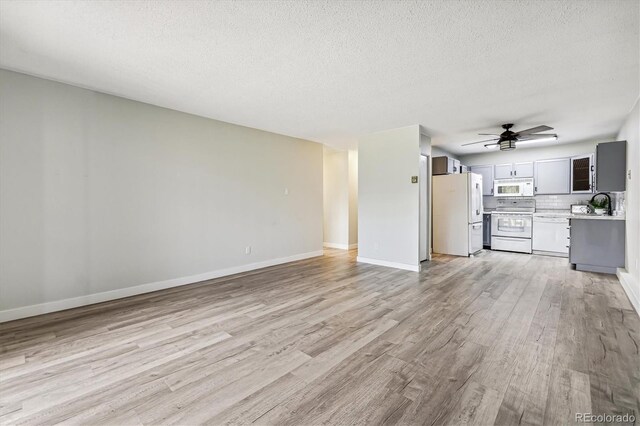 unfurnished living room with sink, light wood-type flooring, ceiling fan, and a textured ceiling