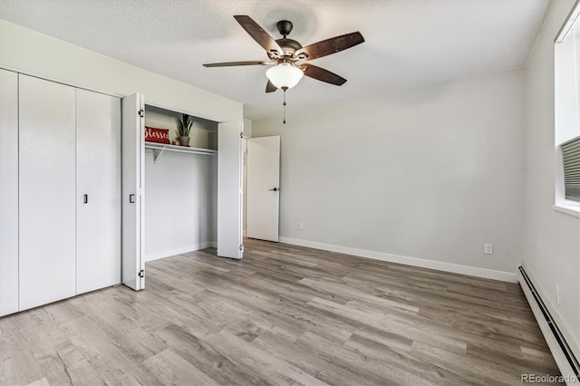 unfurnished bedroom featuring a textured ceiling, baseboards, baseboard heating, light wood-type flooring, and two closets