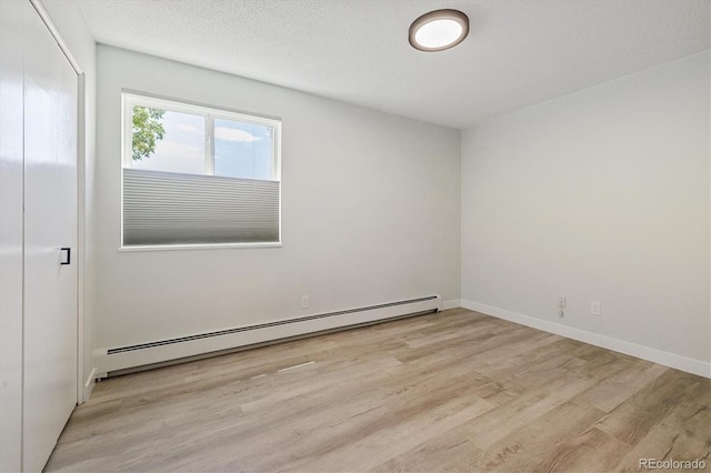 empty room with a textured ceiling, baseboard heating, light wood-type flooring, and baseboards