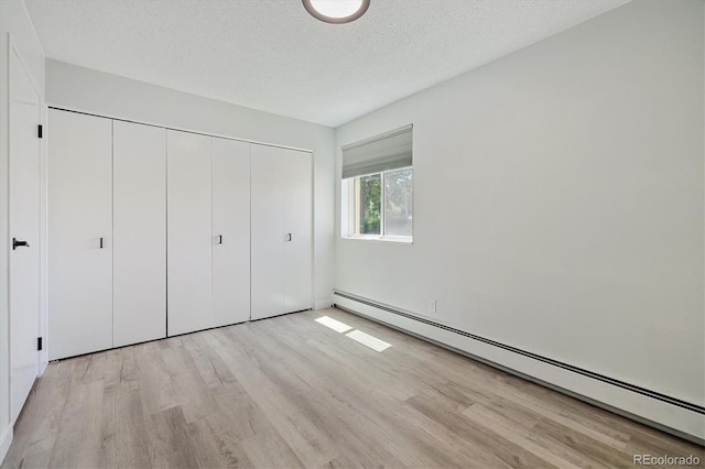 unfurnished bedroom featuring a baseboard radiator, a closet, light wood-style flooring, and a textured ceiling