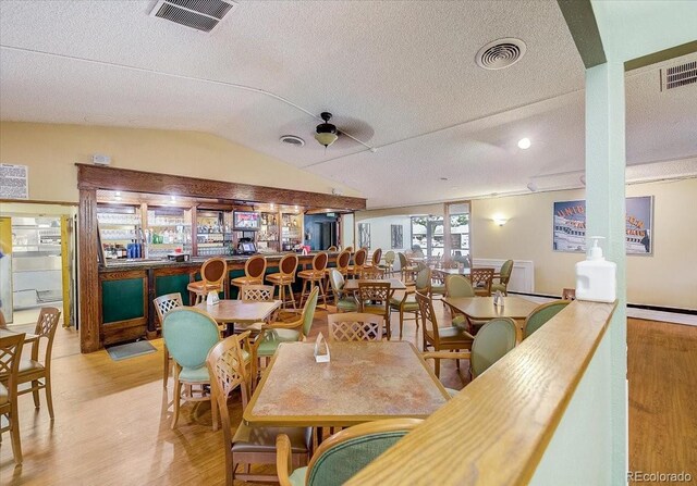 dining area featuring light hardwood / wood-style floors, a textured ceiling, ceiling fan, and vaulted ceiling