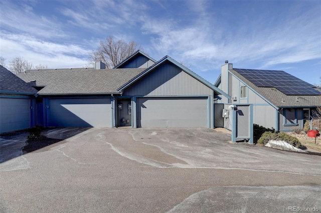 view of front of property featuring a chimney, a shingled roof, roof mounted solar panels, a garage, and driveway