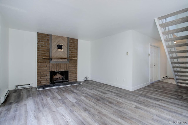 unfurnished living room with a baseboard heating unit, wood finished floors, baseboards, stairway, and a brick fireplace