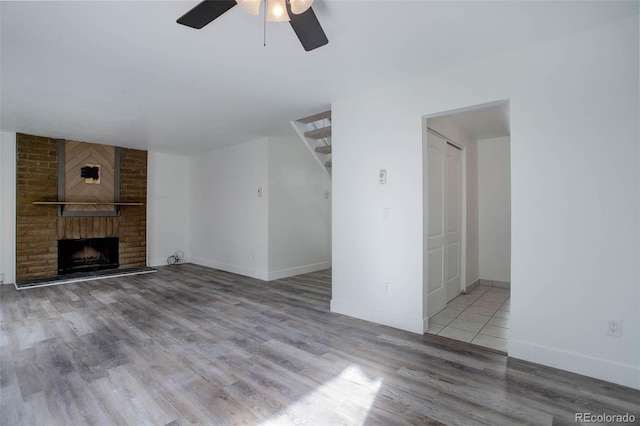 unfurnished living room with ceiling fan, light wood-style flooring, a fireplace, baseboards, and stairway