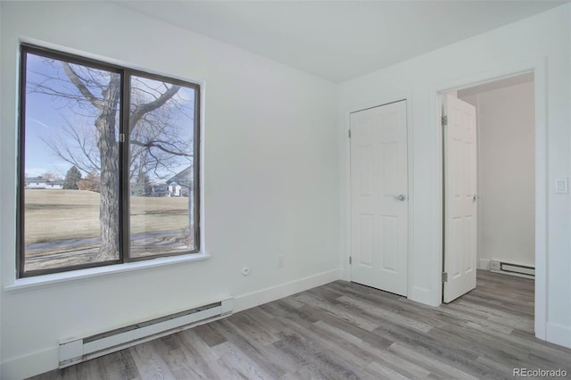 spare room featuring a baseboard heating unit, light wood finished floors, and a wealth of natural light