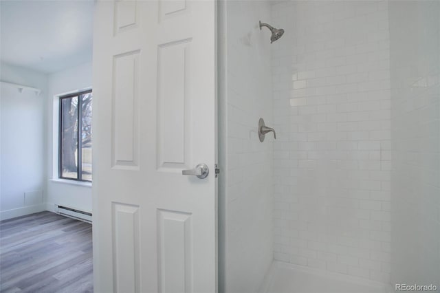 full bath featuring baseboards, baseboard heating, tiled shower, and wood finished floors