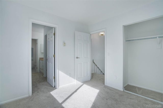 unfurnished bedroom featuring a closet, light carpet, ensuite bath, and baseboards