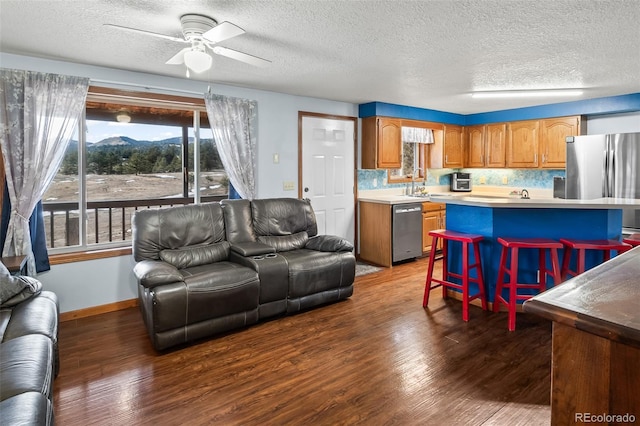 living area featuring a ceiling fan, a textured ceiling, baseboards, and wood finished floors