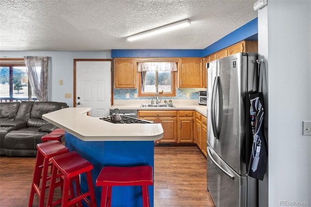 kitchen with open floor plan, freestanding refrigerator, light countertops, a kitchen bar, and a sink