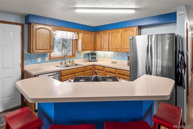 kitchen with stainless steel appliances, a peninsula, a sink, a kitchen breakfast bar, and light countertops