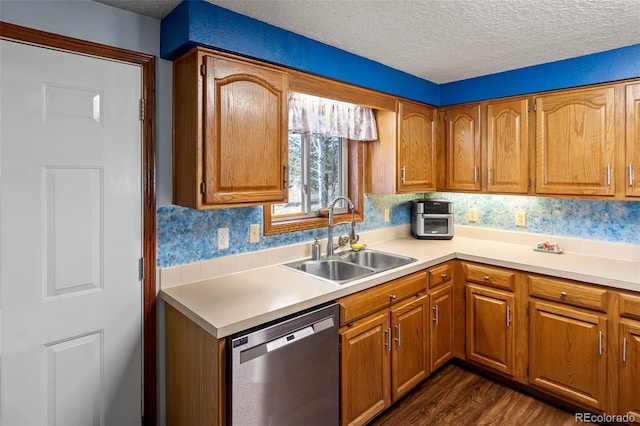 kitchen featuring brown cabinets, light countertops, stainless steel dishwasher, a sink, and a textured ceiling