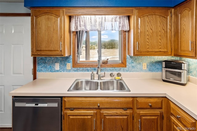 kitchen featuring a sink, light countertops, dishwasher, brown cabinetry, and wallpapered walls