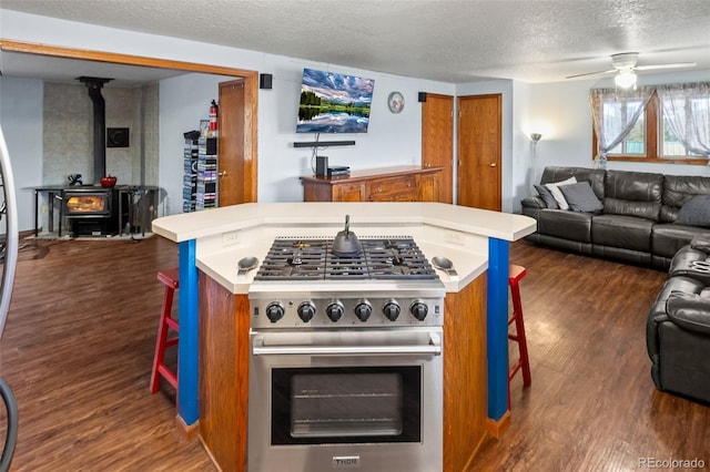 kitchen with a breakfast bar area, gas range, open floor plan, dark wood-style floors, and a wood stove