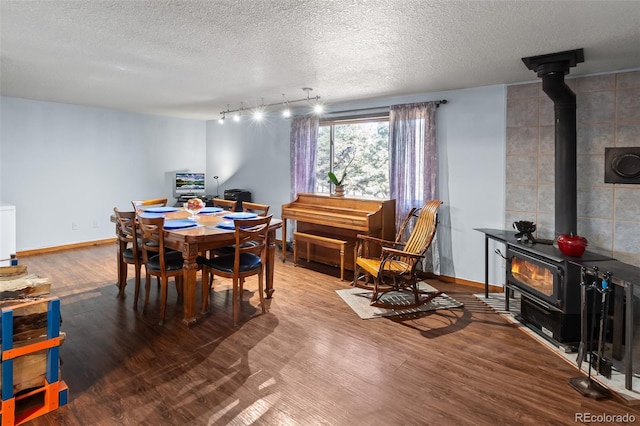 dining area featuring a textured ceiling, wood finished floors, a wood stove, and baseboards