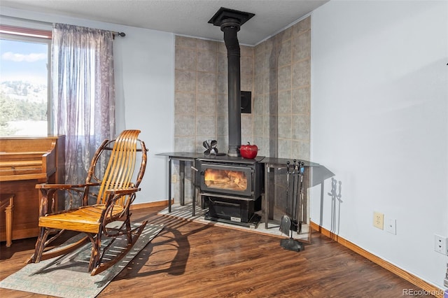 living area featuring tile walls, a wood stove, a textured ceiling, wood finished floors, and baseboards