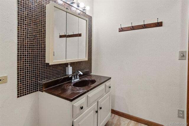 bathroom with baseboards, backsplash, vanity, and wood finished floors