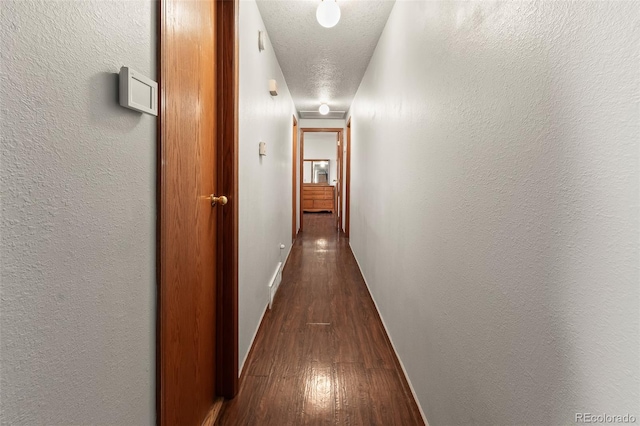 hallway with dark wood-style floors, baseboards, a textured ceiling, and a textured wall