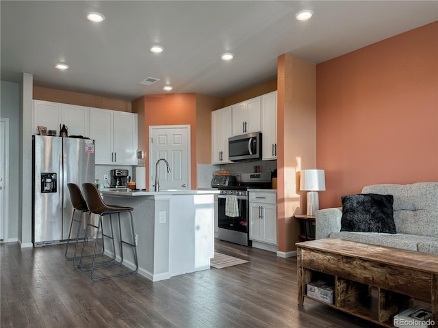 kitchen with stainless steel appliances, white cabinetry, and an island with sink