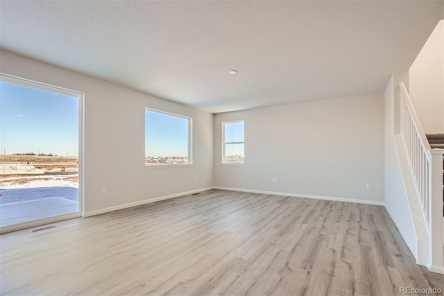 unfurnished room featuring light wood-type flooring, baseboards, and a textured ceiling