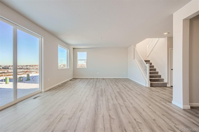 unfurnished living room with stairway, baseboards, and wood finished floors