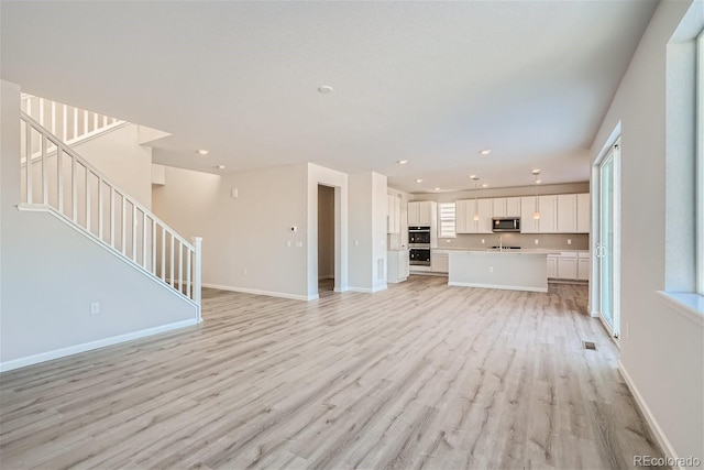 unfurnished living room with light wood-type flooring, stairway, baseboards, and recessed lighting