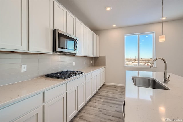 kitchen with stainless steel appliances, a sink, white cabinets, light wood-style flooring, and recessed lighting
