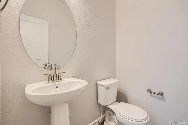 bathroom featuring toilet, a textured wall, and a sink