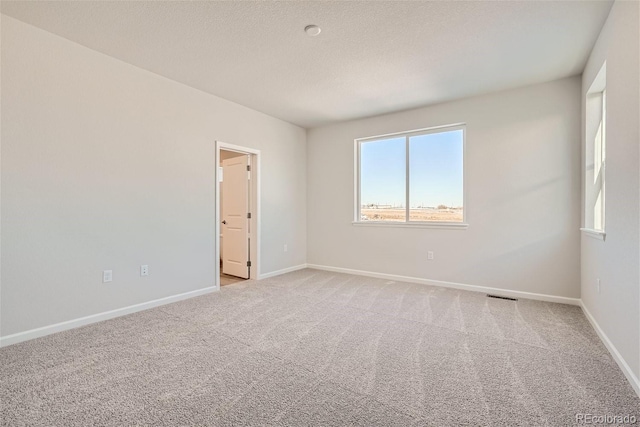 empty room featuring light colored carpet, baseboards, and a textured ceiling