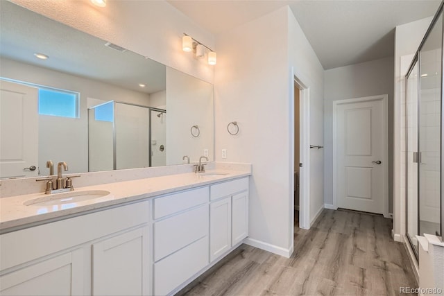 full bath featuring a shower stall, double vanity, wood finished floors, and baseboards