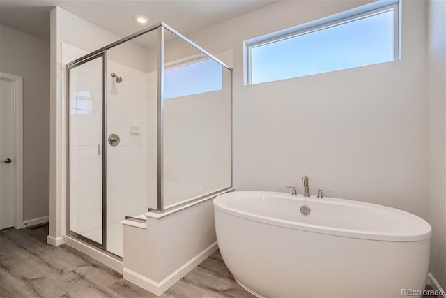 bathroom featuring a stall shower, wood finished floors, a freestanding tub, baseboards, and recessed lighting