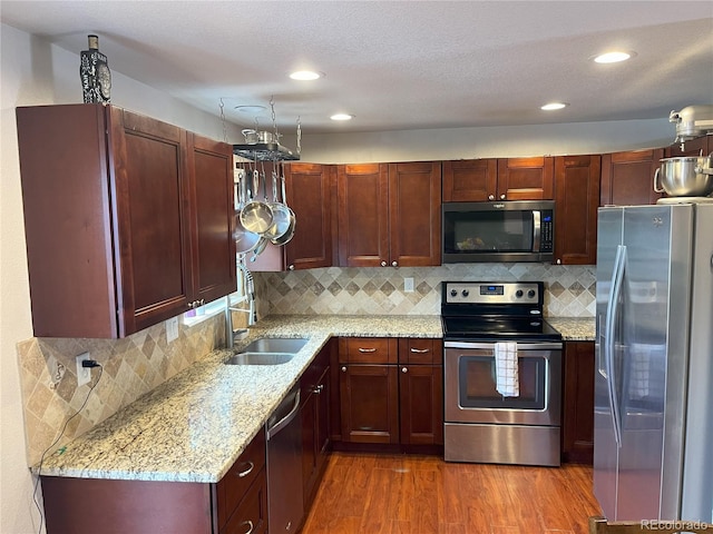 kitchen with stainless steel appliances, sink, light stone countertops, backsplash, and dark wood-type flooring