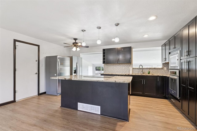108 Olympus Cir, Lone Tree, CO 80124 - kitchen with appliances with stainless steel finishes, light stone countertops, decorative backsplash, a kitchen island, and light wood finished floors