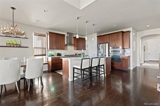 15290 W Baker Ave, Lakewood, CO 80228 - kitchen featuring appliances with stainless steel finishes, wall chimney range hood, arched walkways, light countertops, and a chandelier