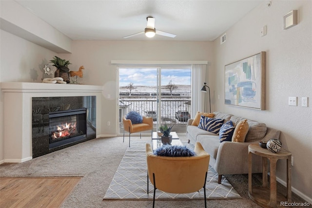 living room featuring ceiling fan, a tiled fireplace, and carpet