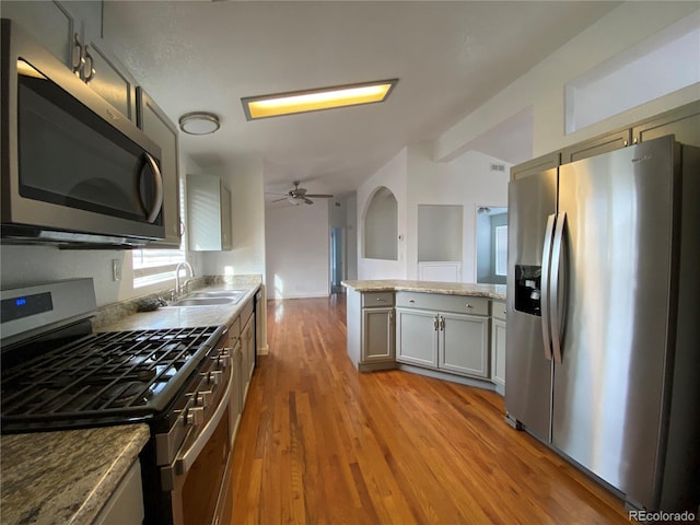 kitchen with ceiling fan, light stone counters, sink, appliances with stainless steel finishes, and light wood-type flooring