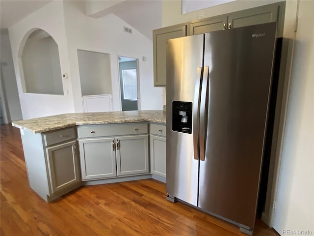 kitchen featuring lofted ceiling, stainless steel fridge, kitchen peninsula, light stone countertops, and hardwood / wood-style floors