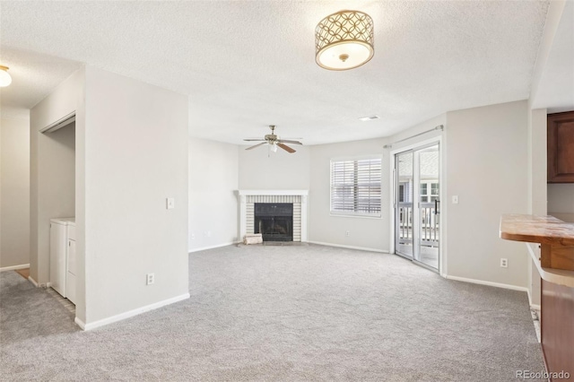 unfurnished living room with separate washer and dryer, a textured ceiling, light carpet, ceiling fan, and a brick fireplace