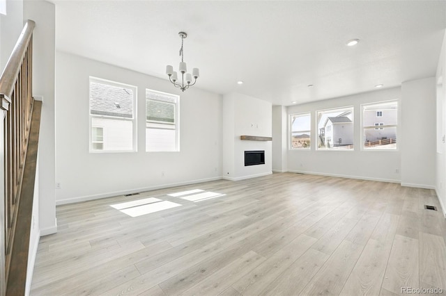 unfurnished living room featuring baseboards, an inviting chandelier, visible vents, and light wood-style flooring