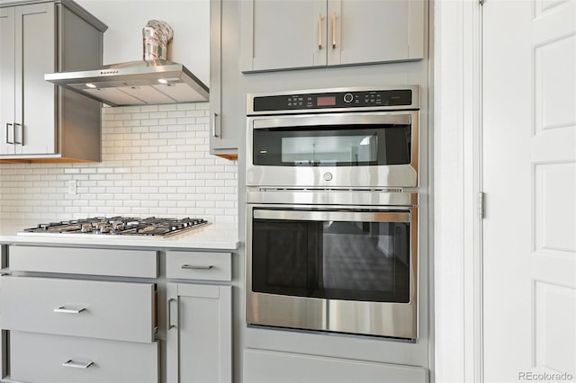 kitchen featuring stainless steel appliances, light countertops, gray cabinets, wall chimney exhaust hood, and tasteful backsplash