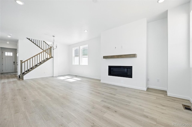 unfurnished living room with light wood-type flooring, baseboards, visible vents, and stairway