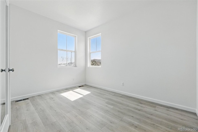 spare room with light wood-type flooring, visible vents, and baseboards