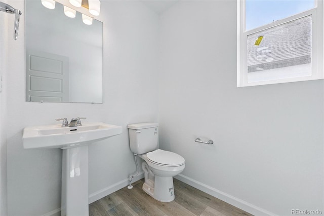 half bath featuring wood finished floors, toilet, baseboards, and a sink