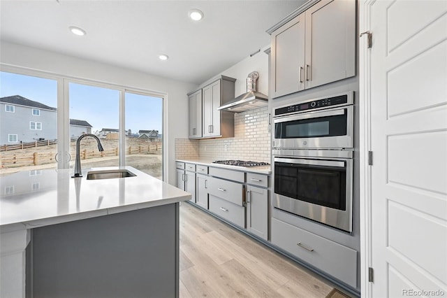 kitchen featuring light wood finished floors, appliances with stainless steel finishes, a sink, and gray cabinetry