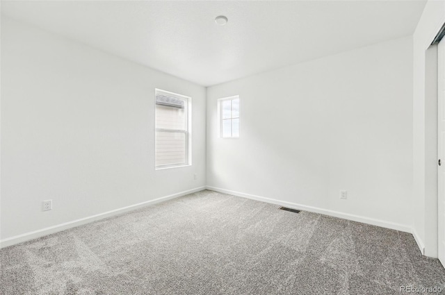spare room featuring carpet floors, visible vents, and baseboards