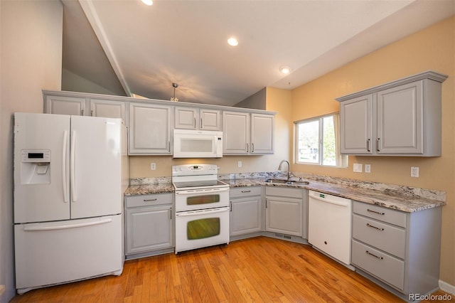 kitchen with white appliances, gray cabinetry, a sink, lofted ceiling, and light wood-style flooring