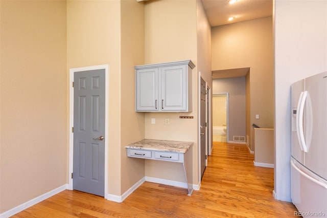hallway featuring light wood-type flooring, a high ceiling, and baseboards