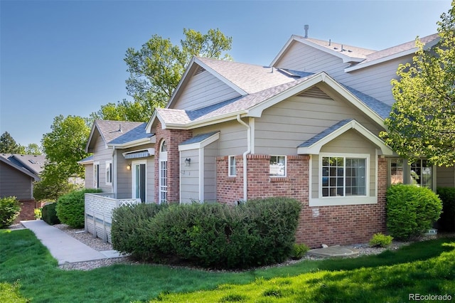 view of home's exterior featuring brick siding, a shingled roof, and a lawn