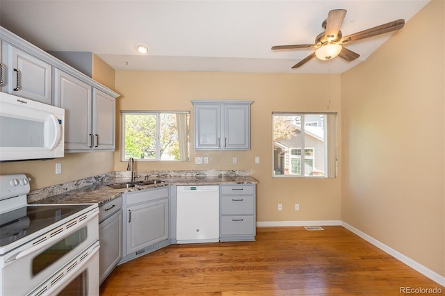 kitchen featuring white appliances, a sink, light wood finished floors, baseboards, and ceiling fan